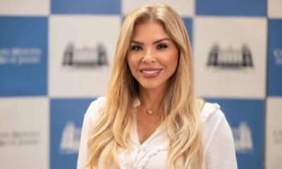 Veronica Costa sorri diante de um painel azul e branco
