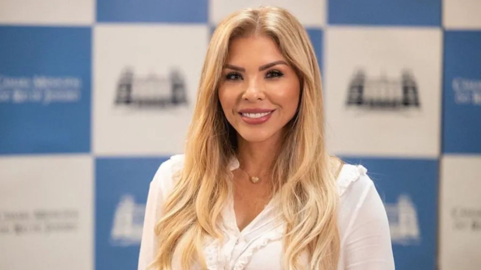 Veronica Costa sorri diante de um painel azul e branco