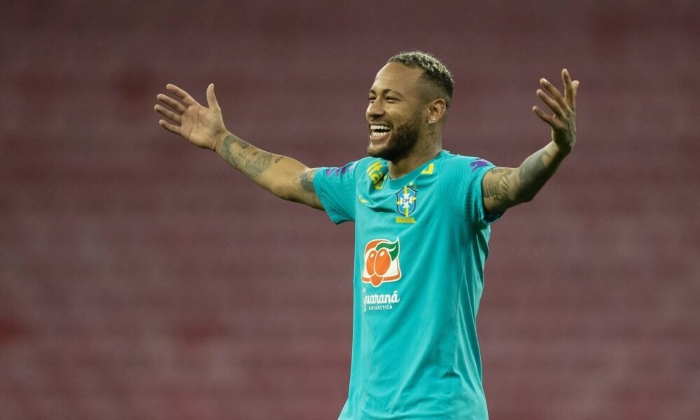 Neymar sorrindo com os braços abertos e camisa de treino da seleção brasileira.