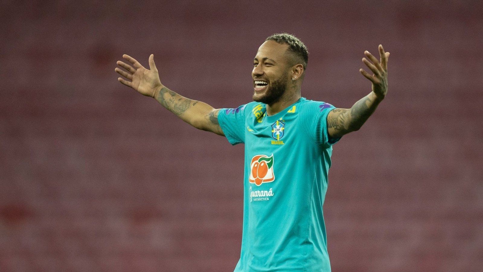 Neymar sorrindo com os braços abertos e camisa de treino da seleção brasileira.