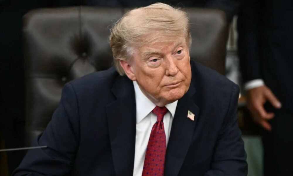 Donald Trump sentado, com terno azul-marinho e gravata vermelha.
